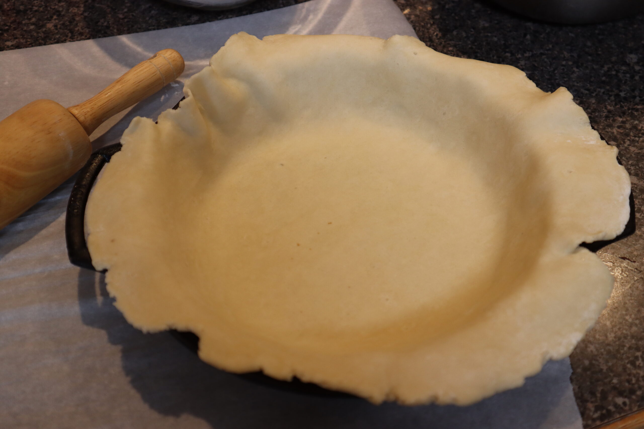 Homemade Pie Crust rolled out into a cast iron pie dish with a rolling pin beside it