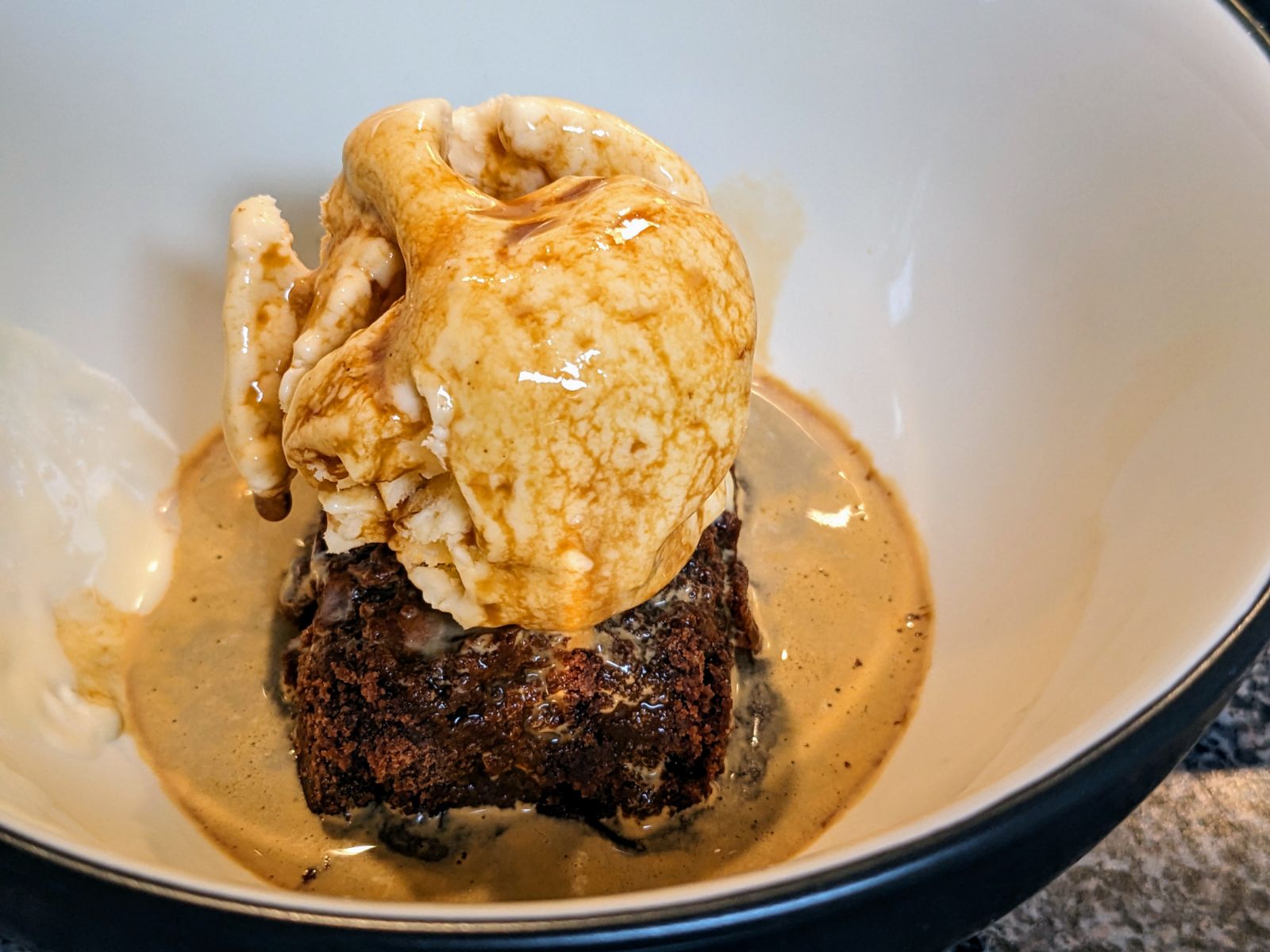 Affogato with Chocolate brownie with vanilla ice cream on top with a hot shot of espresso poured on top in a white bowl with graphite colored rim