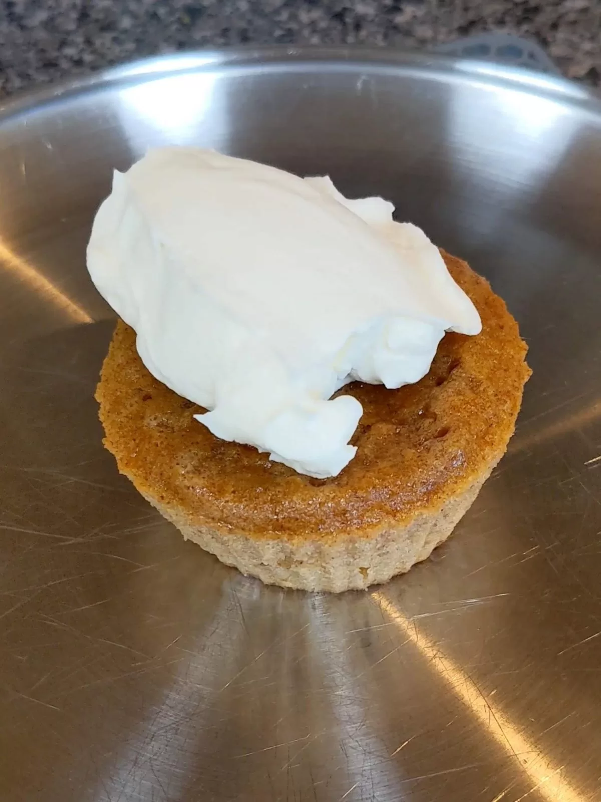 homemade whipped cream on top of a pumpkin pie cupcake on a stainless steel plate