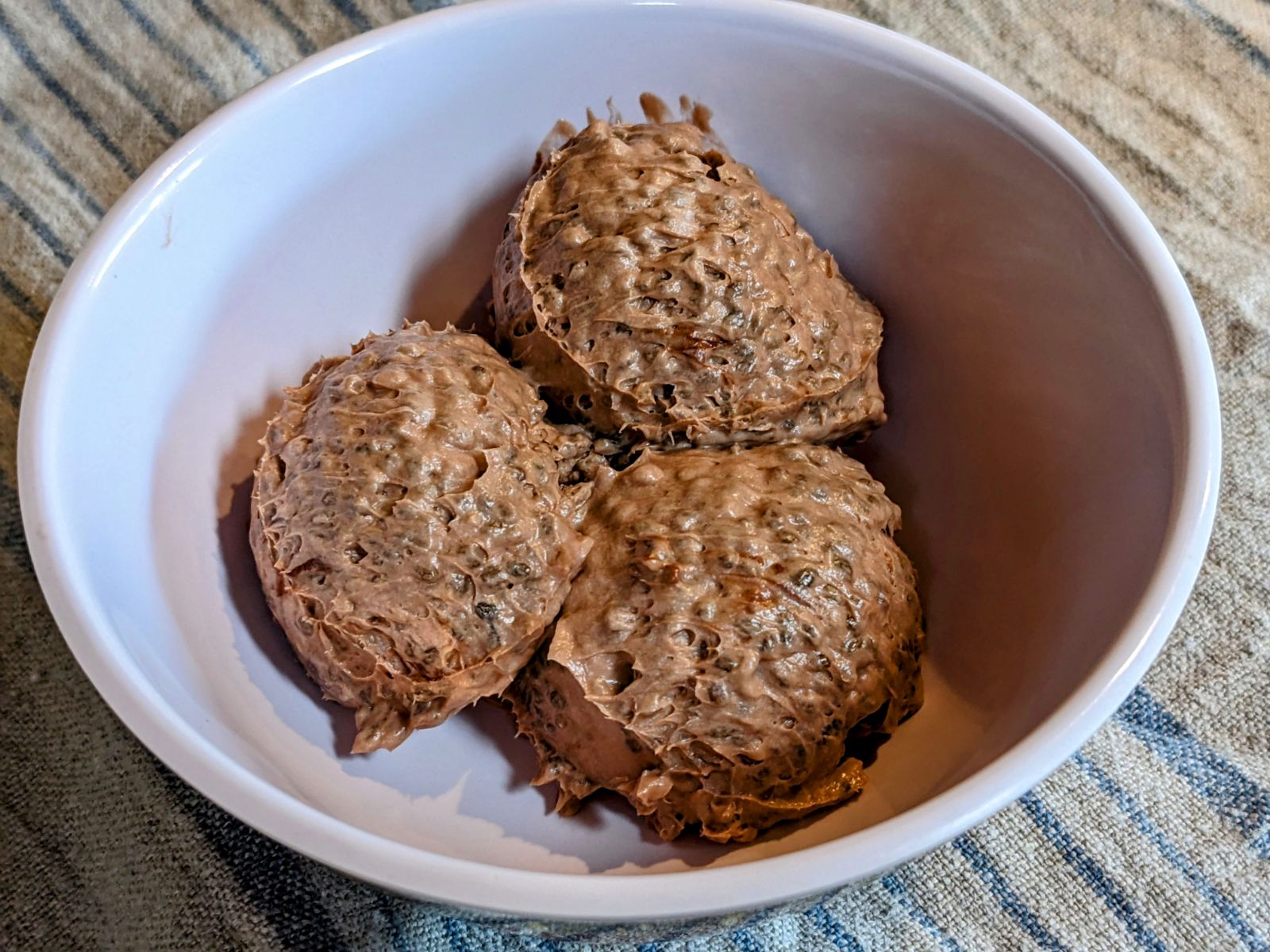 3 scoops of chocolate chia pudding in a white bowl on top of a gray and blue striped linen towel