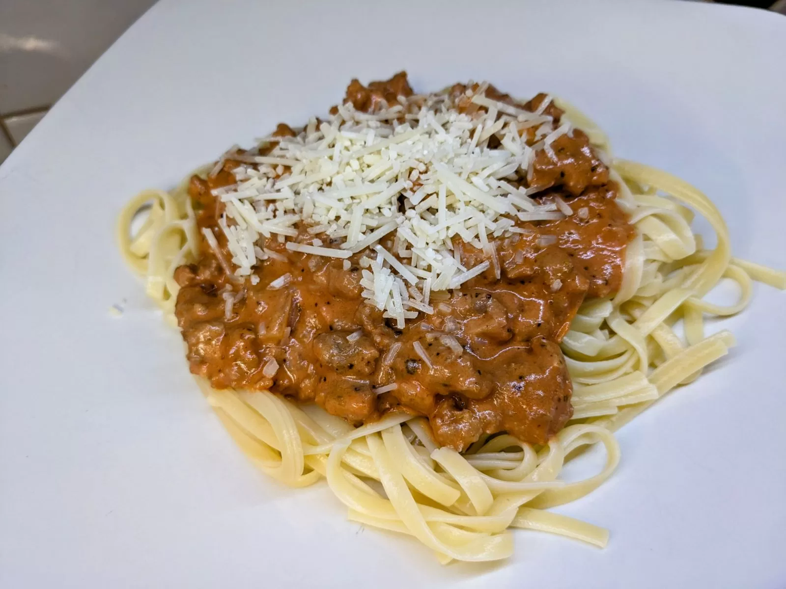 italian sausage in a tomato cream sauce over linguine on a white plate